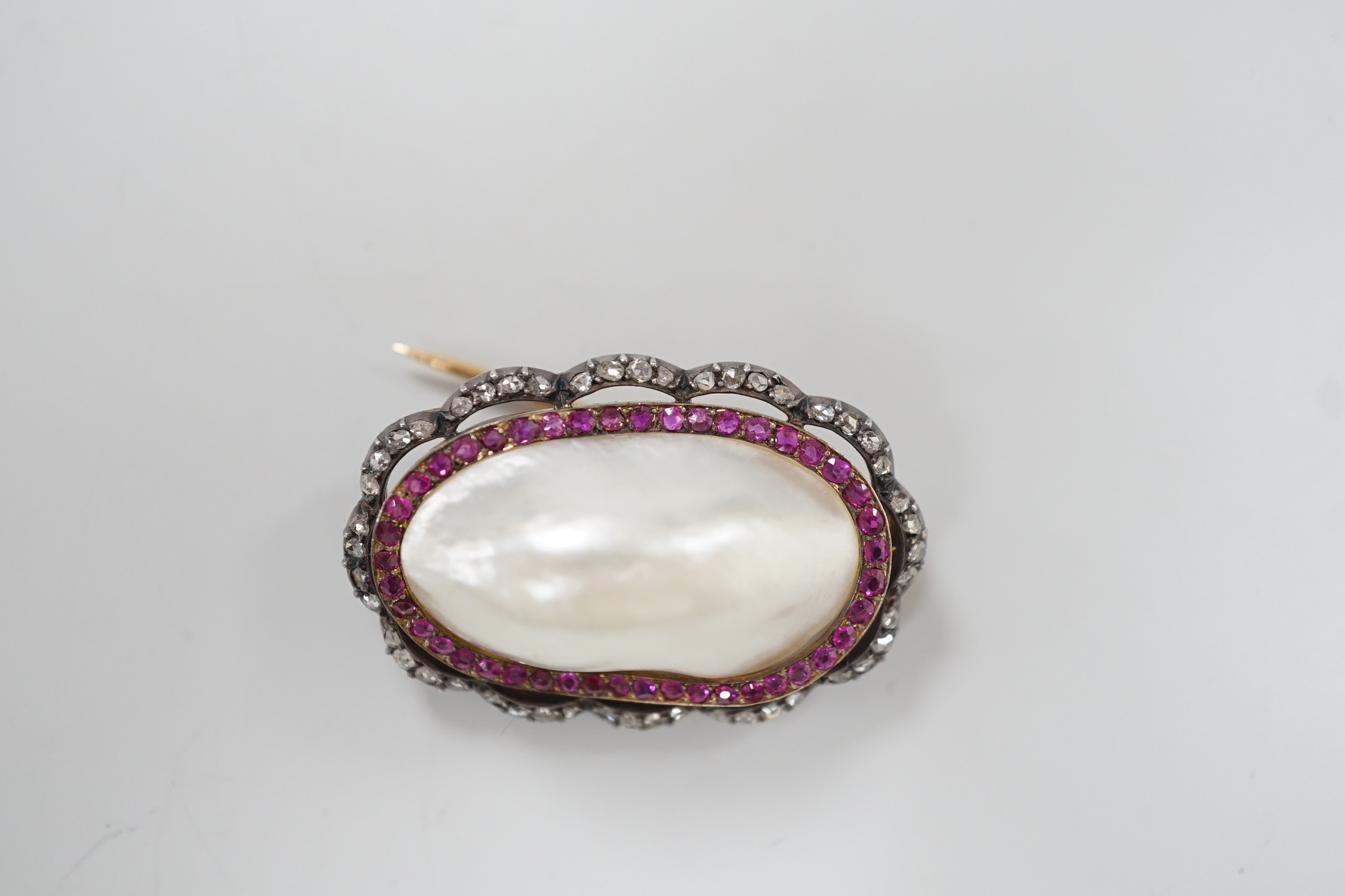 An early 20th century French yellow metal (18ct poincon mark on pin), white metal and mabe pearl set oval brooch, bordered by concentric rows of rubies and rose cut diamonds, 38mm, gross weight 17.3 grams.